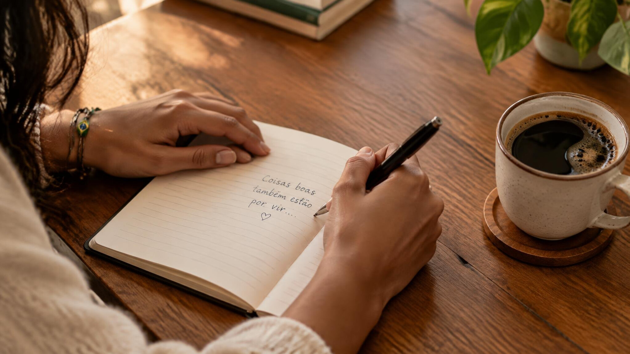 Pessoa escrevendo uma mensagem em um caderno perto de uma xícara de café